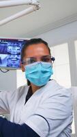 POV of patient in a dental clinic sitting on surgery chair checking affected mass. Dentistry team working in orthodontic office, lighting the lamp and examining person, close-up face in medical mask. photo