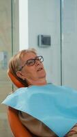 Close up of patient wearing dental bib talking with dentist before intervetion. Orthodontist speaking to woman with toothache sitting on stomatological chair while nurse preparing sterilized tools. photo