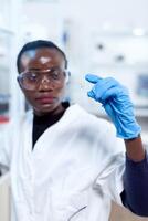 Close up of african biochemists holding microscope sample on glass slide with protective gloves. Black healthcare scientist in biochemistry laboratory wearing sterile equipment. photo