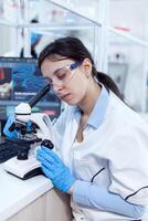 Scientist in protective eyewear doing virus experiment using microscope. Medical technician wearing white coat in sterile laboratory doing solution analysis. photo