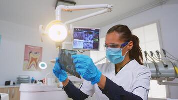 Dentist customizing light over the chair and analysing teeth x-ray before surgery. Dentistry doctor lighting the lamp and examining person wearing protection mask and glasses, nurse helping her photo