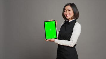 Asian restaurant hostess showing greenscreen display in studio, presenting isolated mockup layout on tablet. Waitress working with blank copyspace chromakey template on screen. Camera A. photo