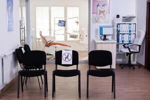 Empty waiting area, stomatology reception with nobody in it with new normal having sign on chair for social distance during covid-19 epidemic. Dental waiting room modern equipped in outbreak time photo