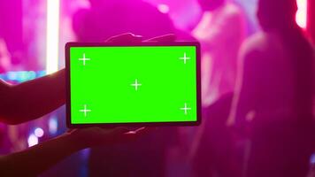 Person showing tablet with greenscreen at nightclub, being on the dance floor holding device with mockup template. Girl looking at isolated chroma key display with blank copyspace. photo