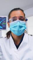 Patient point of view to dentist in protective mask holding tools examining person with toothache sitting on stomatological chair while nurse preparing tools for surgery. photo