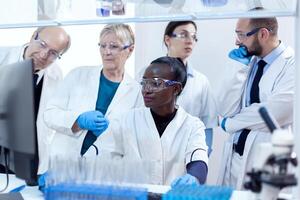 Chemists biologists conducting medical analysis using computer. African healthcare researcher in biochemistry laboratory wearing sterile equipment. photo