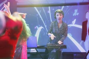 Excited woman dj mixing music using jog wheels on controller while performing on nightclub stage portrait. Young musician playing at discotheque party in club and looking at camera photo