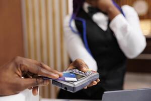 Hospitality and NFC technology. Close up of male hand holding credit card paying for room during check-in at front desk, receptionist receiving cashless payment from guest in hotel photo