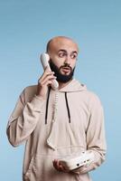 Arab man answering landline phone call and looking away with surprised expression. Young person talking on old fashioned corded telephone, having conversation, listening to interlocutor photo