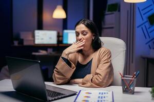 Exhausted businesswoman yawning working on important project in financial firm. Smart woman sitting at her workplace in the course of late night hours doing her job. photo