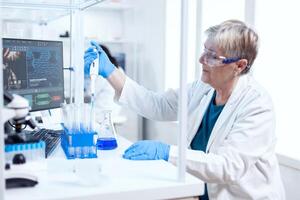 Senior scientist filling test tube wearing protective equipment using molecular dispenser. People in innovative pharmaceutical laboratory with modern medical equipment for genetics research. photo