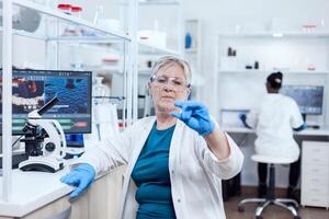 Senior scientist in modern laboratory holding genetic sample on laboratory glass. Elderly researcher in sterile lab looking on microscope slide wearing lab coat. photo