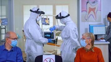 hombre que se discute con enfermero en dental recepción vistiendo proteccion traje en contra coronavirus, mayor pacientes esperando en recepción acuerdo distancia. concepto de nuevo normal dentista visitar en brote. foto