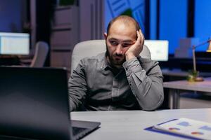 cansado empresario sentar a el computadora el noche trabajos en fecha límite. trabajador obsesivo empleado que cae dormido porque de trabajando tarde a noche solo en el oficina para importante empresa proyecto. foto