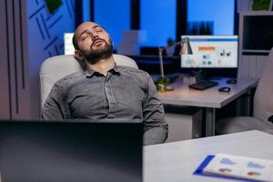 Exhausted hardworking businessman sleeping on chair. Workaholic employee falling asleep because of working late at night alone in the office for important company project. photo