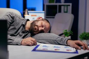 trabajo duro empresario duerme en mesa a lugar de trabajo porque de fecha límite. trabajador obsesivo empleado que cae dormido porque de mientras trabajando tarde a noche solo en el oficina para importante empresa proyecto. foto