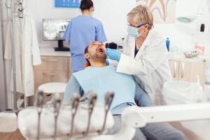 Dentistry senior woman doctor making professional teeth cleaning to sick man patient during orthodontic consultation in dental office. Hospital team examining toothache preparing tooth treatment photo