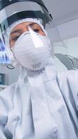 Patient pov of dentist holding dental tools wearing covid protection suit treating patient in new normal clinic. Stomatolog wearing safety gear against coronavirus during heatlhcare check of person. photo