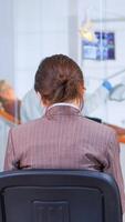 Back view of woman filling in dental form sitting on chiar in waiting room preparing for dental implants while doctor exemination patient in background. Crowded professional orthodontist office. photo