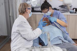 dentista grupo de doctores con médico cara mascaras utilizando profesional dental herramientas durante estomatológico cirugía en odontología hospital oficina habitación. ortodoncista médico trabajando a cuidado de la salud tratamiento foto