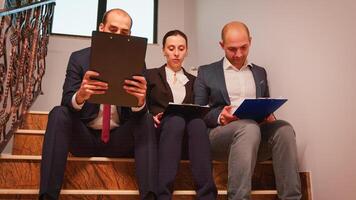 Team of business people making plans analysing annual graphs enjoying sitting on staircase explaining finance project. Group of company manager and office executive on busy stairs of workplace. photo