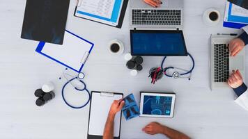 Doctors checking x-ray from top view flatlay sitting on desk with stethoscope and digital device having medical conference. Team of physicians working in clinic on copy space using modern technology. photo