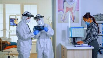 lento movimiento de estomatológico doctores con en general mirando a radiografía en esperando área, planificación cirugía durante global pandemia mientras mayor pacientes que se discute sentado en sillas acuerdo distancia. foto