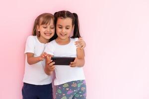two little girls with a smartphone on a pink background photo
