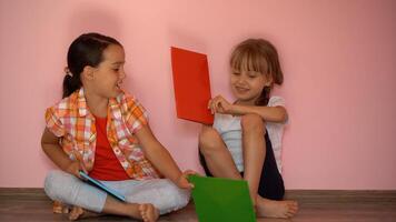 Lovely little girls are reading a book. The concept of education. Isolated on pink background photo