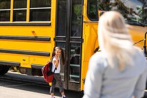 Kids student running into mother's hands to hug her after back to school near the school bus photo