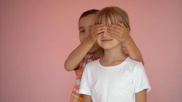 Portrait of two cute friends 7 years old girl Covering Eyes Isolated over pink background photo