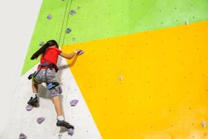 Sporty little girl climbing artificial boulder on practical wall in gym photo