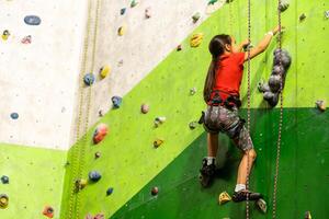 Sporty little girl climbing artificial boulder on practical wall in gym photo