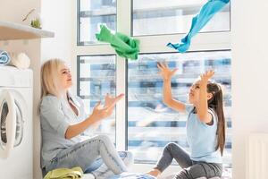 family mother and child girl little helper in laundry room near washing machine and dirty clothes photo