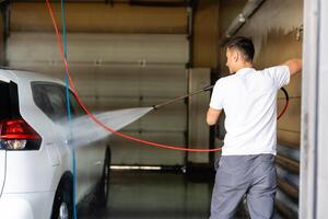 Young tall man spalshing his car by garden hose photo
