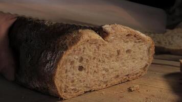 Cutting slice of homemade Crusty rye bread with a sharp knife on wooden board, closeup slow motion video