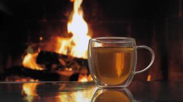 Glass mug with fruit tea against background of a fireplace with a flame. Fresh hot herbal tea with mint and oranges, detox drink. video