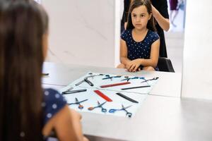 Portrait of pretty little girl seating at table with accessories in a hairdressing salon photo