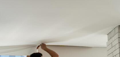 Process of installing stretch ceiling in the hall. Close up of the hand of man with a tool. photo