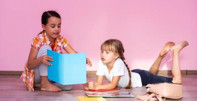 Little girls reading a book in living room. Smart schoolgirls doing their homework after school. Education and distance learning for kids. Homeschooling during quarantine. Stay at home entertainment. photo