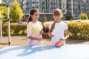 joven adolescente niña jugando silbido apestar. ella sostiene un pelota y un raqueta en su manos. jugando mesa tenis al aire libre en el yarda foto