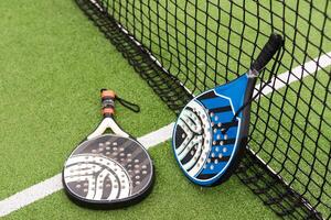 Yellow balls on grass turf near padel tennis racket behind net in green court outdoors with natural lighting. Paddle is a racquet game. Professional sport concept with copy space. photo