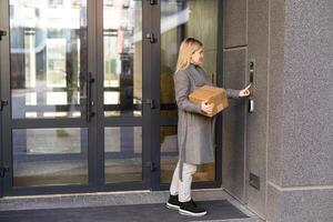 Happy woman ringing on doorbell at building entrance. Using intercom photo