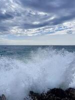 a large wave crashing against the rocks on a cloudy day photo