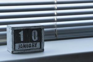 Mañana enero 10 en de madera calendario en pie en ventana con persianas foto