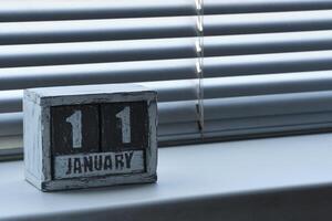 Morning January 11 on wooden calendar standing on window with blinds. photo