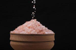 Pouring pink salt into wooden cup black background. photo