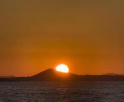 sunset over the sea with a mountain in the background photo