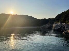 the sun is setting over the water in front of a rocky shore photo