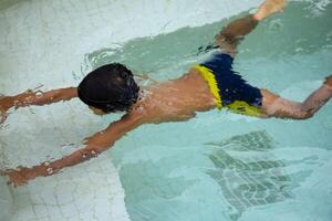 Happy Indian boy swimming in a pool, Kid wearing swimming costume along with air tube during hot summer vacations, Children boy in big swimming pool. photo